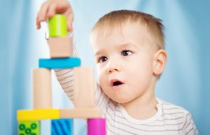 Portrait of a two years old child stacking wooden cubes. Pretty little boy on blue background