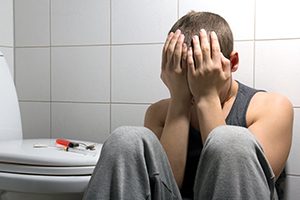 Young stoned man with heroin addiction sitting in bathroom