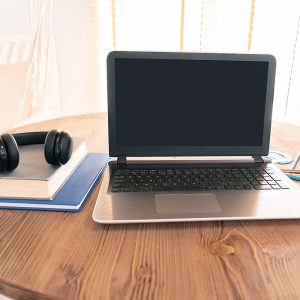 Laptop notebook with blank screen and headphones and books on wooden table.