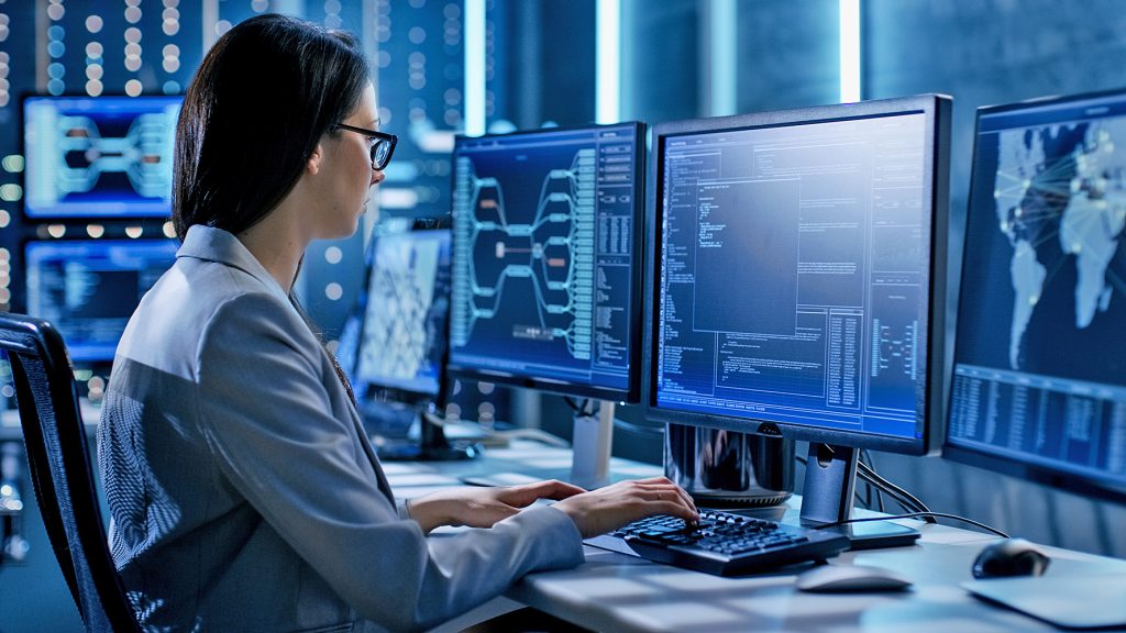 Photo of woman sitting at computer with several monitors
