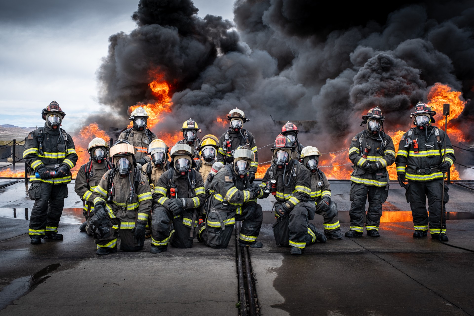 Photo of Fire & Rescue Academy students in full fire-fighting gear, posing in front of fire and smoke at the State Fire Marshal's Academy in Socorro, NM